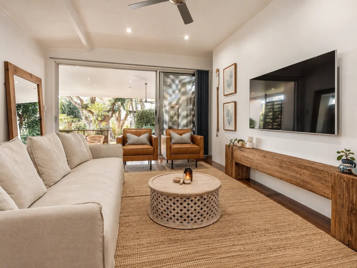 Not Nothing Beach House: living room with a linen sofa, carved round coffee table, leather armchairs and doors to the deck