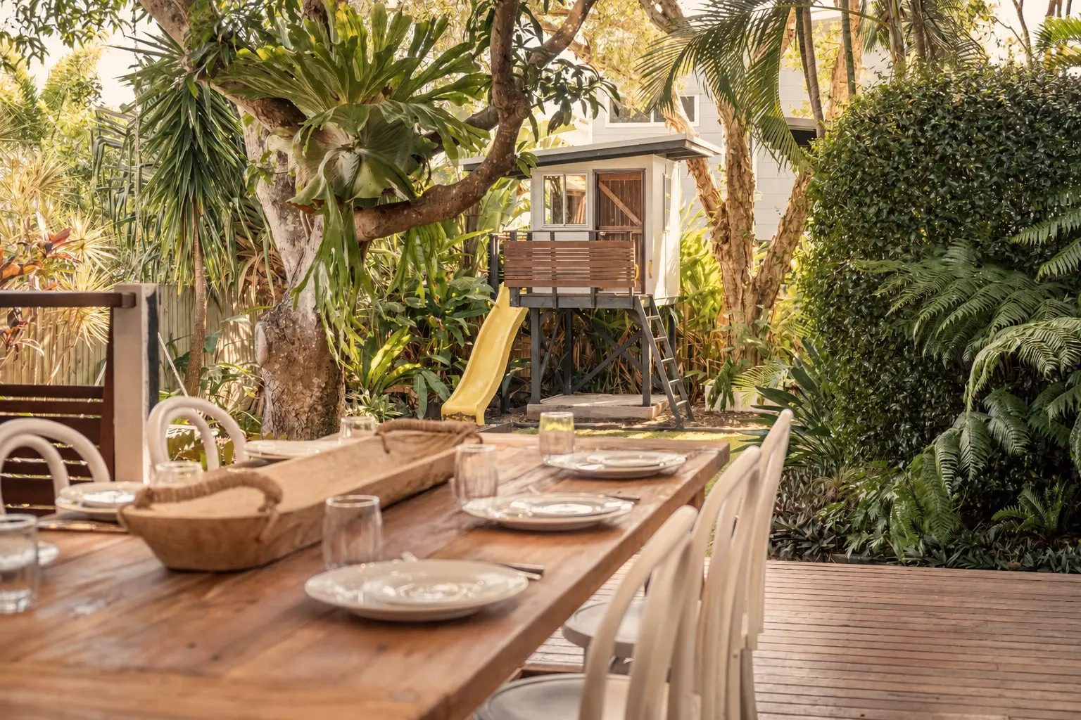 Not Nothing Beach House: dining table set for guests on the deck, beside a treehouse and lush garden