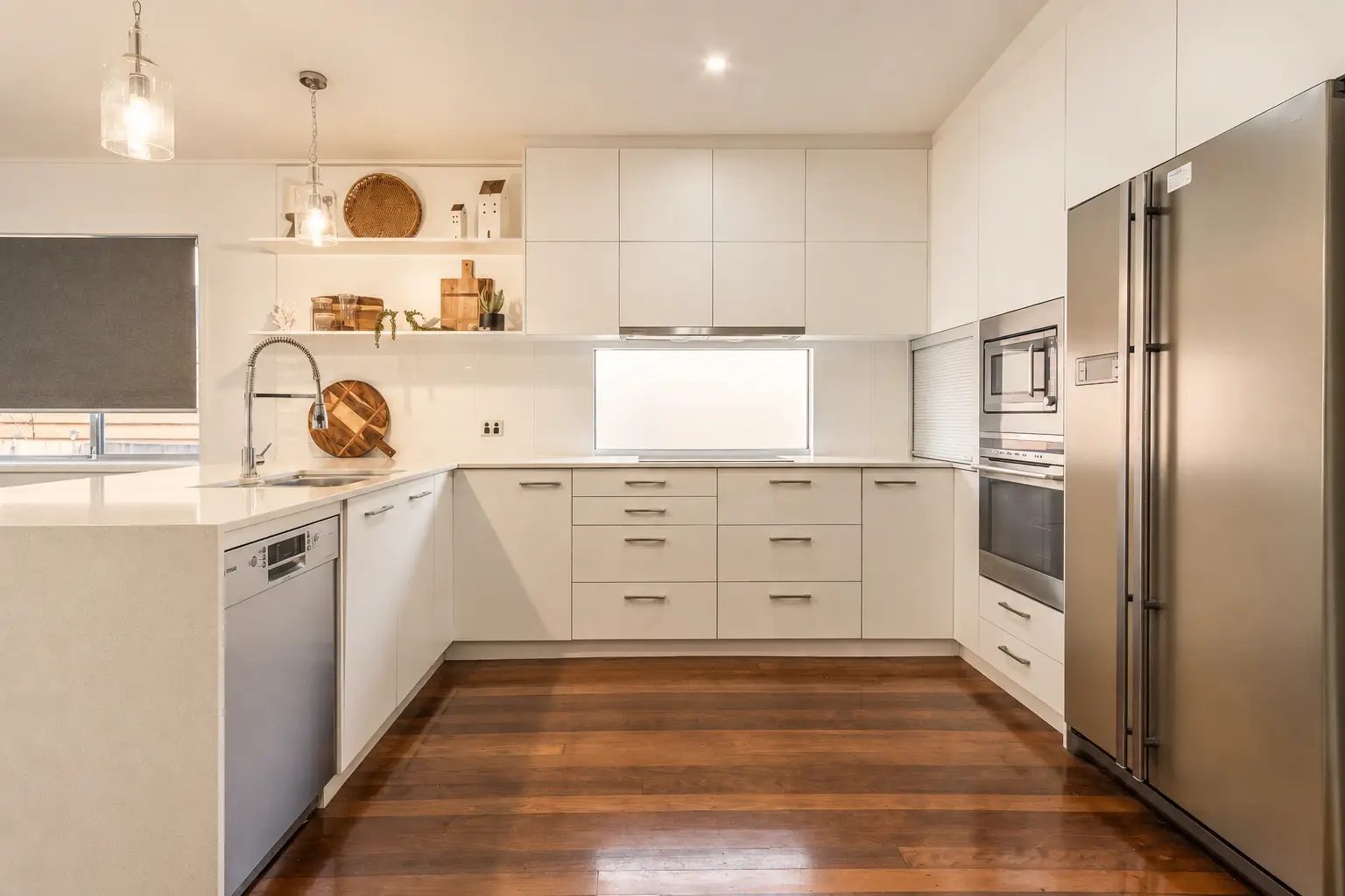 Not Nothing Beach House: white u-shaped kitchen with stainless appliances and warm recycled timber floors